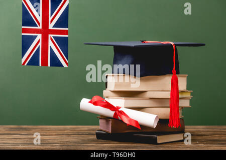 Bücher, akademische Kappe, Diplom und Britische Flagge auf Holz- Oberfläche isoliert auf Grün Stockfoto