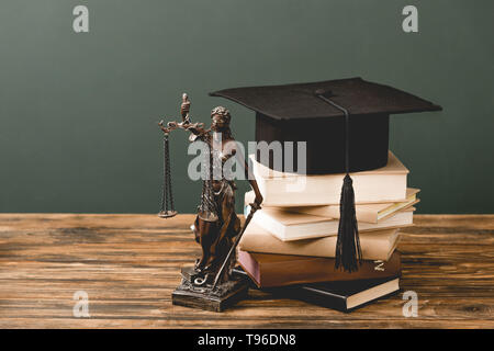 Themis Statuette, Bücher und akademischen Kappe auf Holz- Oberfläche isoliert auf Grau Stockfoto