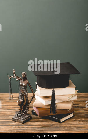 Themis Statuette, Bücher und akademischen Kappe auf Holz- Oberfläche isoliert auf Grau Stockfoto