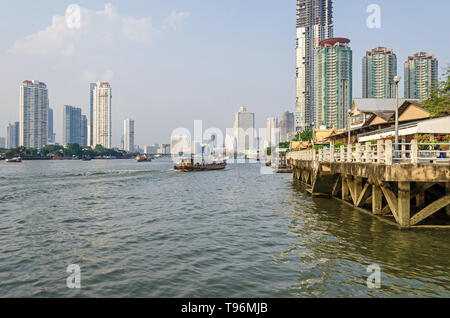 Bangkok, Thailand - 18 April 2018: Chao Phraya Fluss mit Booten, Taksin Brücke und ihre modernen Gebäuden - Chatrium Hotel Riverside, State Tower mit Stockfoto