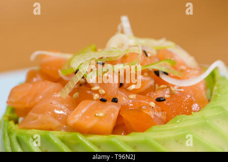 Tartar Lachs Fleisch in Scheiben Avocado gewickelt, garniert mit dünnen Schichten von Lauch, Schwarz und Weiß Sesam auf einer weißen Platte Stockfoto