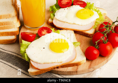 Sandwich mit Schinken, Rührei, Tomate, Salat, leckeren, gesunden Frühstück und Orangensaft auf weißem Holz- Hintergrund Stockfoto