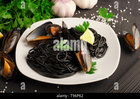 Meeresfrüchte schwarzer Pasta Spaghetti mit Muscheln auf weiße Platte auf dunklem Hintergrund. Mediterrane Delikatesse Essen Stockfoto