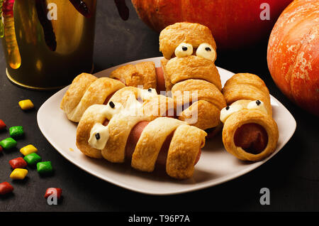 Beängstigend wurst Mumien im Teig mit lustigen Augen mit Süßigkeiten und Kürbis Stockfoto