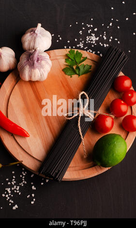 Schwarze Spaghetti mit Zutaten zum Kochen Pasta auf schwarzem Hintergrund Stockfoto