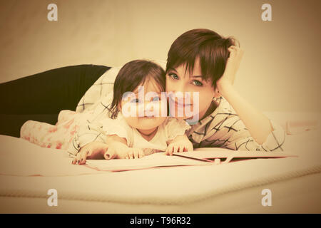 Glückliche junge Mutter und Baby Mädchen das Lesen eines Buches auf dem Bett Stockfoto