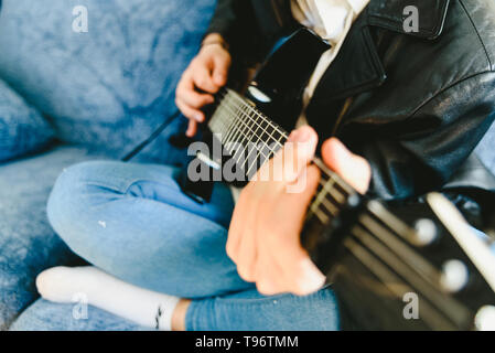 Junger Mann, der mit seiner E-Gitarre auf dem Sofa seines Hauses lernen. Stockfoto