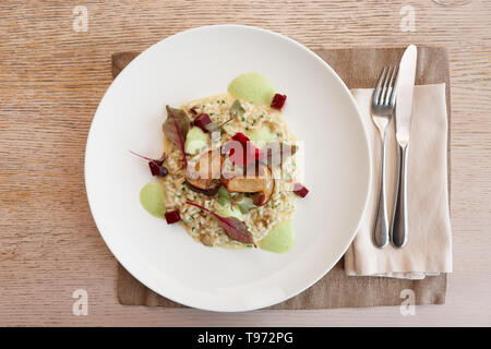 Risotto mit gebratenen Steinpilzen auf Platte, Gedeck im Restaurant Stockfoto