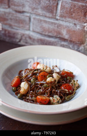 Roggen Pasta mit Kapern und Garnelen in weißem Porzellan Teller gegen die Wand Stockfoto