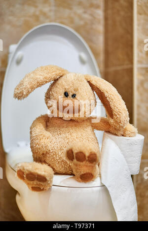 Weich gefüllte Kaninchen mit Toilettenpapier auf der Toilette. Das Konzept von Verdauungsproblemen. Stockfoto