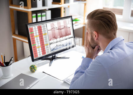 Verzweifelten Geschäftsmann mit finanziellen Verlusten an seinem Schreibtisch consulting Graphen sitzen auf Monitoren konfrontiert Stockfoto
