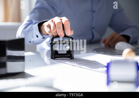 Nahaufnahme von einer Person Hand Stanzen mit Genehmigt Stempel auf Dokument am Schreibtisch Stockfoto