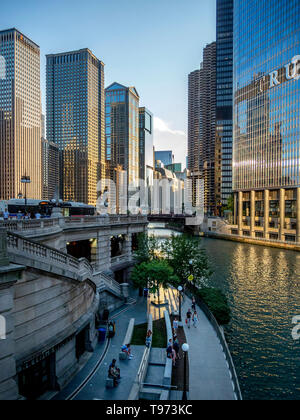 Moderne Bürogebäude am Ufer des Chicago River an der North Michigan Avenue spiegeln die Nachmittagssonne als Fußgänger auf einem Uferweg entfernt. Stockfoto