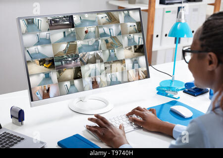 Junge Geschäftsfrau Kontrolle CCTV-Kamera Aufnahmen auf Computer über Schreibtisch im Büro Stockfoto