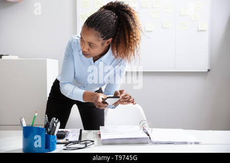 Close-up ist eine junge geschäftsfrau Hand, Foto, Dokument über Handy heimlich im Büro Stockfoto