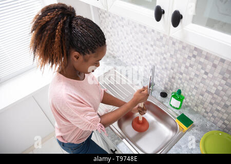 Seitenansicht eines weiblichen Klempner mit Kolben In der Spüle Stockfoto