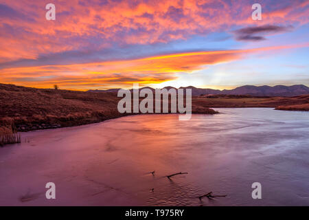 Sonnenuntergang Winter Lake - eine bunte winter Sonnenuntergang an einem zugefrorenen Bergsee. Bear Creek Park, Denver-Lakewood, Colorado, USA. Stockfoto