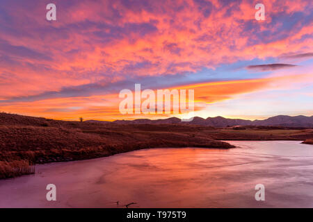 Brennender Himmel über einen zugefrorenen See - leuchtend roten Sonnenuntergang Himmel über einen gefrorenen Bergsee. Bear Creek Park, Denver-Lakewood, Colorado, USA. Stockfoto