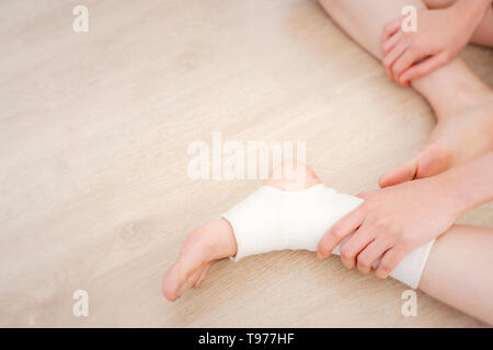 Closeup Menschen von einem Fuß mit weißer Gaze Elastische Bandage. Hände auf verletzte Beine und Füße auf den Schmerz. Asiatische junge Frau Knöchelverletzung Runner Sitzen Stockfoto