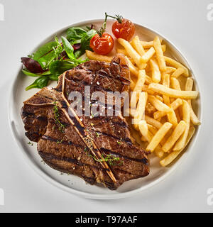 Lecker gegrilltes oder gegrillten T-Bone-Steak mit gebratenen Pommes frites, Salat und gebratene Tomaten von oben über Weiß im quadratischen Format angezeigt Stockfoto