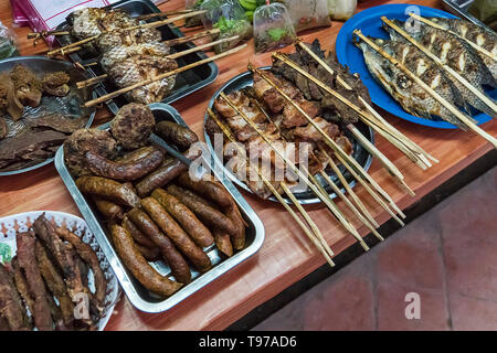 Straße Nahrungsmittel in Laos, ausgewählte konzentrieren, Grill. Verschiedene Arten von Fisch, Fleisch und andere Lebensmittel auf den Zähler auf dem Tisch. Street Food in Asien. Stockfoto