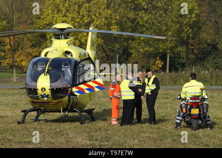 Niederländische Ambulance Hubschrauber (Lifeliner 1) steht auf Gras in Almere Stad, während ein Pilot und Polizei officiers neben dem Gesetz Flugzeuge stehen. Stockfoto