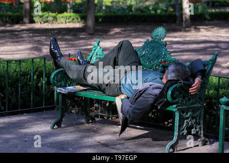 Der Mann, der um 12.00 Uhr auf einer Bank im Park schläft Stockfoto