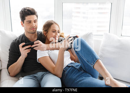 Portrait von europäischen Paar Mann und Frau mit Handys, während auf der Couch im hellen Zimmer zu Hause liegen Stockfoto