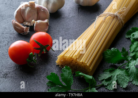 Ungekochte spaghetti Pasta mit Seil aus Sackleinen mit Cherry Tomaten, Knoblauch und frischen Zweigen der grünen Koriander auf schwarzem Hintergrund Stockfoto