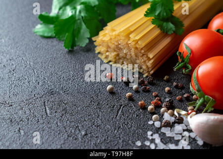 Auf einem schwarzen Hintergrund nehmen die Hälfte der Frame raw Spaghetti mit frischem Koriander Blätter, mehrere Tomaten, Knoblauchzehe, Pfeffer und grobem Meersalz Stockfoto