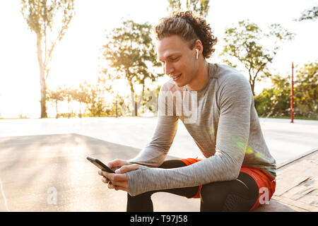 Lächelnd Sportler tragen Ohrhörer mit Handy beim Sitzen im Freien Stockfoto