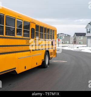 Klar Square Seitenansicht eines School Bus auf einer Straße, die durch verschneite Häuser im Winter Stockfoto