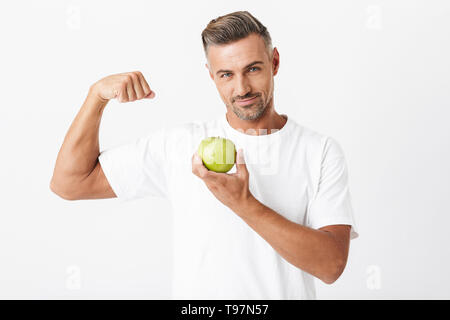 Bild Der unrasierte Mann 30 s mit Borsten legere T-Shirt seinen Bizeps auf Kamera und mit Apfel isoliert auf weißem Hintergrund Stockfoto