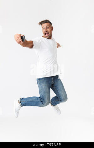 Volle Länge Bild Der unrasierte Mann 30 s legere t-shirt Holding und über Handy auf weißem Hintergrund Stockfoto