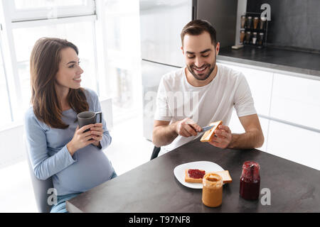 Portrait von schönen Familie glücklich Menschen und schwangere Frau Frühstück im Haus, während bei Tisch und in der Küche sitzt Stockfoto
