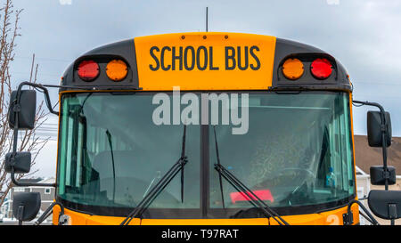 Klar Panorama Vorderansicht eines gelben Schulbus mit Wohnungen und bewölkter Himmel im Hintergrund Stockfoto