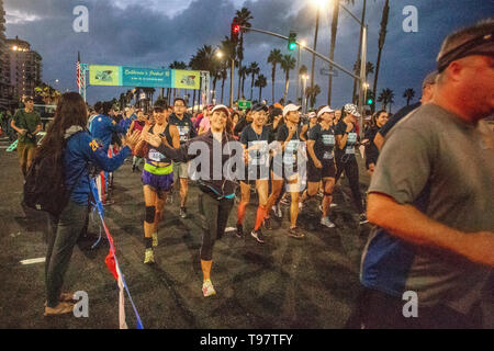 Ein Läufer erhält ein ermutigendes Hand smack als Newport Beach, CA, 10K Rennen den Start in der Morgendämmerung Dunkelheit verlässt. Stockfoto