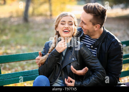 Liebevolle junge Paare sitzen auf Holzbank im Herbst Park Stockfoto