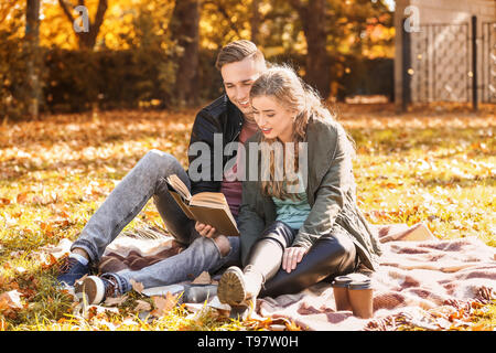 Liebevolle junge Paar lesen Buch über Plaid im Herbst Park Stockfoto