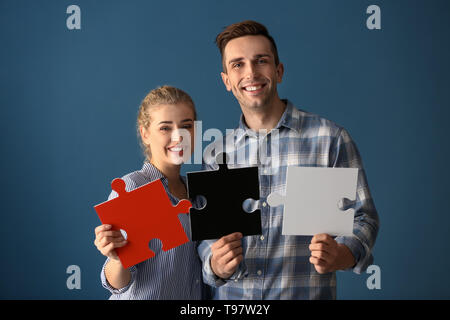 Junges Paar mit Stücken von Puzzle auf farbigen Hintergrund Stockfoto