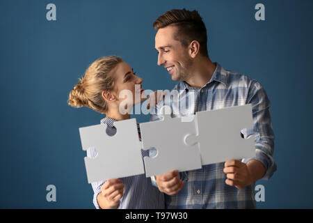 Junges Paar mit Stücken von Puzzle auf farbigen Hintergrund Stockfoto