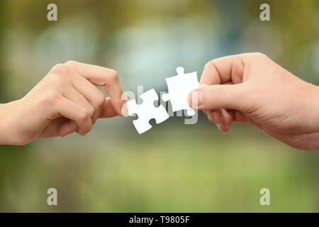 Männliche und weibliche Hände mit Stücken von Puzzle auf unscharfen Hintergrund Stockfoto