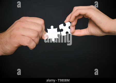Männliche und weibliche Hände mit Stücken von Puzzle auf dunklem Hintergrund Stockfoto