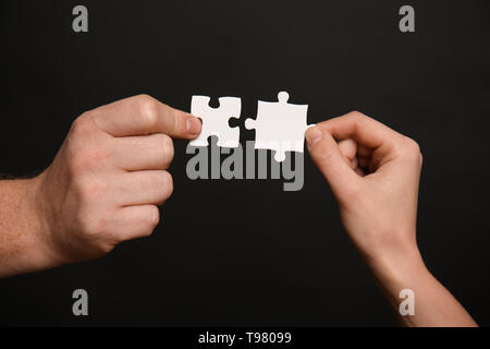 Männliche und weibliche Hände mit Stücken von Puzzle auf dunklem Hintergrund Stockfoto