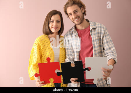Junges Paar mit Stücken von Jigsaw Puzzle auf farbigen Hintergrund Stockfoto