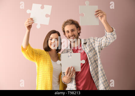 Junges Paar mit Stücken von Jigsaw Puzzle auf farbigen Hintergrund Stockfoto