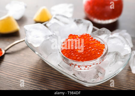 Schüssel mit köstlichen roten Kaviar und Eiswürfel auf hölzernen Tisch Stockfoto