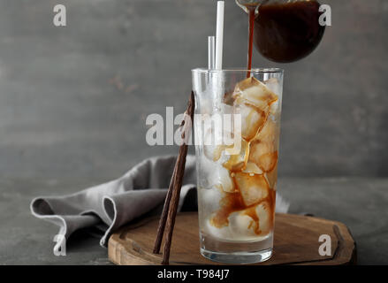 Gießen Kaffee aus der Kanne in Glas mit Eiswürfeln auf Tisch Stockfoto