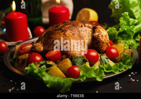 Weihnachten Teller. Xmas gebackene ganze Hähnchen mit Tomaten und Kartoffeln close-up auf einem Schild an einem Tisch mit Kerze Stockfoto
