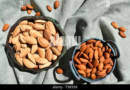 Mandel in Keramik Schüssel. Ungeschälte Nüsse in der Schale tief grüne rustikale Porzellan. Organische Rohstoffe gesunde Ernährung. Top Nahaufnahme Leinen Stoff niemand Stockfoto